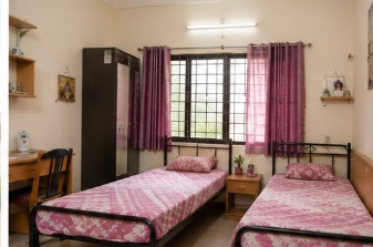 Premium twin room at Sairam Ladies Hostel with floral bedding and purple curtains