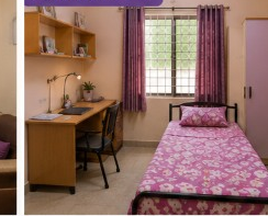 Single room at Sairam Ladies Hostel with study desk, floral bedding, and lavender curtains